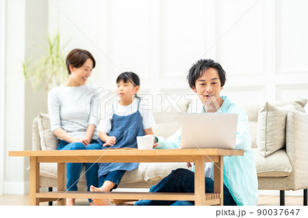 家族のいるリビンで仕事をする男性。 90037647