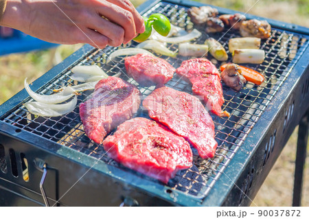 屋外で金網に載せて焼く肉にスパイスを振るバーベキューのクローズアップ 屋外で金網に載せて焼く肉にスパイスを振るバーベキューのクローズアップ 90037872