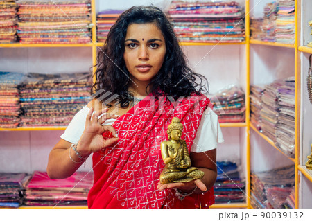 business lady indian seller tradition red sari souvenir shop buddha shiva figurine yoga meditation.girl in india in the religion store.beautiful woman with bijouterie jewelry earrings Delhi Bazaar 90039132
