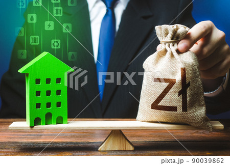 Businessman puts polish zloty money bag on scales and green house. Investment in renovation. Reduced CO2 emissions, energy efficiency. Payback period. Profitability housing of eco technologies. Businessman puts polish zloty money bag on scales and green house. Investment in renovation. Reduced CO2 emissions, energy efficiency. Payback period. Profitability housing of eco technologies. 90039862