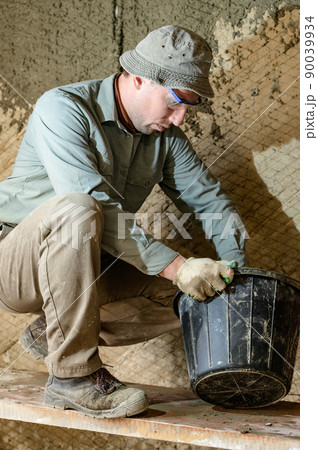 Black bucket with liquid mortar for the first layer of plaster for the wall. Black bucket with liquid mortar for the first layer of plaster for the wall. 90039934