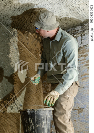 A man throws concrete mortar on the wall, the first layer of plaster on the wall, repair work in Ukraine. 90039935