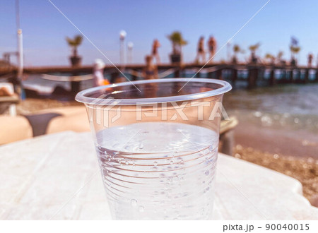 a plastic glass is on the table, a transparent carbonated drink is poured inside. non-ecological packaging, plastic cup pollutes the environment. vacation on the beach a plastic glass is on the table, a transparent carbonated drink is poured inside. non-ecological packaging, plastic cup pollutes the environment. vacation on the beach 90040015