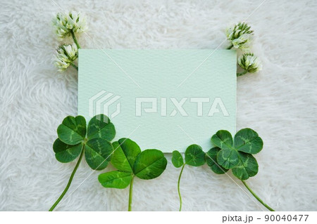 白い布の背景に二つ葉、三つ葉、四つ葉と五つ葉のクローバーと花を飾った緑のカードのタイトルスペース 90040477