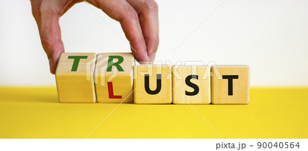Lust or trust symbol. Businessman turns wooden cubes and changes the words 'lust' to 'trust'. Beautiful yellow table, white background. Business and lust or trust concept, copy space. Lust or trust symbol. Businessman turns wooden cubes and changes the words 'lust' to 'trust'. Beautiful yellow table, white background. Business and lust or trust concept, copy space. 90040564