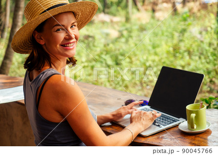 Technology and travel. Working outdoors. Freelance concept. Pretty young woman in hat using laptop in cafe on tropical beach.Hooray victory success and successful deal concept promotion at work Technology and travel. Working outdoors. Freelance concept. Pretty young woman in hat using laptop in cafe on tropical beach.Hooray victory success and successful deal concept promotion at work 90045766