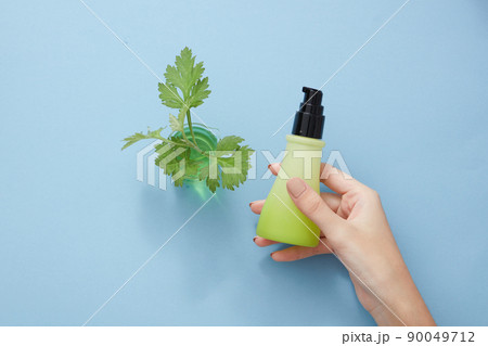 Top view of hand holding cosmetic jar with mugwort in blue background 90049712