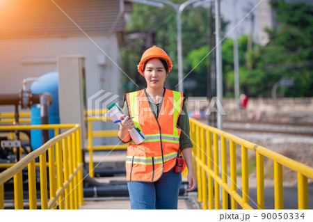 Worker wearing safety uniform under checking the  waste water treatment pond industry ,she used radio communication to connect with another worker in  large to control water support industry. 90050334