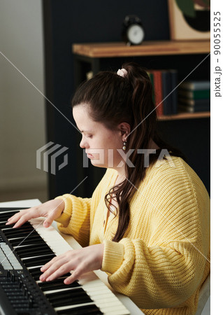 Vertical shot of talented young Caucasian woman with Down syndrome wearing casual clothes spending time at home playing electronic piano Vertical shot of talented young Caucasian woman with Down syndrome wearing casual clothes spending time at home playing electronic piano 90055525
