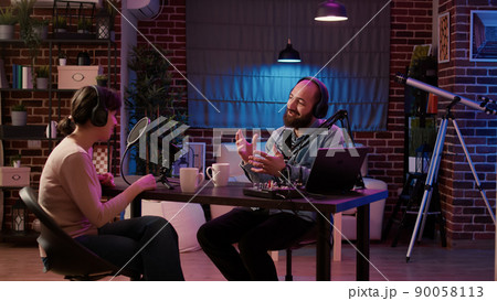 Man and woman talking in online podcast using professional recording equipment having casual conversation in home studio. Radio show host broadcasting interview with influencer using audio mixer. 90058113