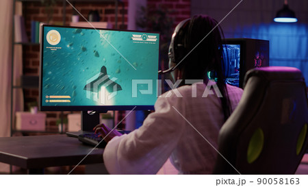 Over shoulder view of african american gamer girl playing space shooter simulation using pc gaming setup enjoying free time at home. Woman streaming online action game multiplayer competition. Over shoulder view of african american gamer girl playing space shooter simulation using pc gaming setup enjoying free time at home. Woman streaming online action game multiplayer competition. 90058163