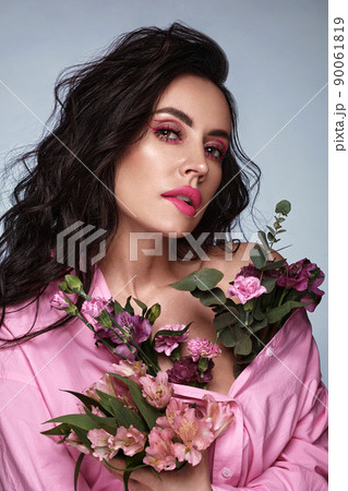 Beautiful brunette girl iwith a gentle pink romantic make-up, pink lips, holding flowers. The beauty of the face. Beautiful brunette girl iwith a gentle pink romantic make-up, pink lips, holding flowers. The beauty of the face. 90061819