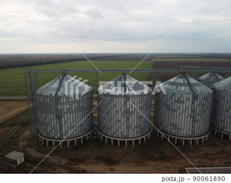 Grain elevator. Metal grain elevator in agricultural zone. Agriculture storage for harvest. Grain elevators on green nature background. Exterior of agricultural factory. Nobody. Grain elevator. Metal grain elevator in agricultural zone. Agriculture storage for harvest. Grain elevators on green nature background. Exterior of agricultural factory. Nobody. 90061890