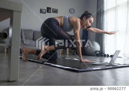 Asian woman doing yoga in front of laptop in living room Asian woman doing yoga in front of laptop in living room 90062277