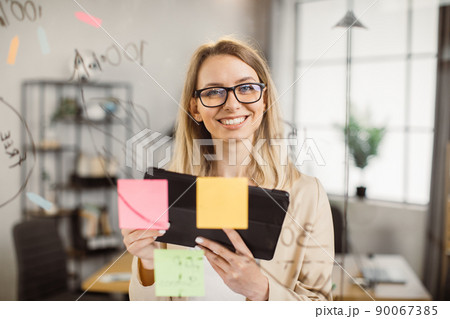Female office worker with tablet standing near glass board Female office worker with tablet standing near glass board 90067385