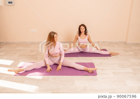 Two beautiful women cook doing yoga, sports together in the gym. Dressed in pink suits. The concept of grace and beauty of the body. 90067596
