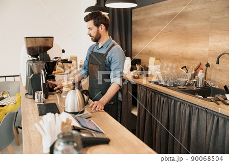 Handsome barista grinds coffee beans in coffeemachine 90068504