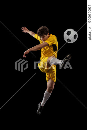 Dynamic portrait of professional football, soccer player training with ball isolated on dark background. Concept of sport, match, active lifestyle, goal and hobby 90069002