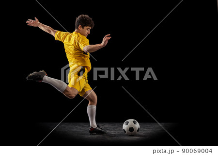 Dynamic portrait of professional football, soccer player training with ball isolated on dark background. Concept of sport, match, active lifestyle, goal and hobby Dynamic portrait of professional football, soccer player training with ball isolated on dark background. Concept of sport, match, active lifestyle, goal and hobby 90069004