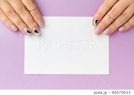 Close up womans hand with creative nail design holding postcard 90070633