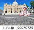 Baby girl sitting on a european city street. Little child outdoors in a town. 90070725