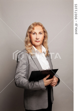 Portrait of mature businesswoman 60s holding black folder on grey background Portrait of mature businesswoman 60s holding black folder on grey background 90071105