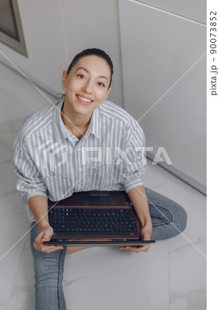 Beautiful girl sitting at home. Woman in a bue blouse. Lady with laptop in her hands. 90073852