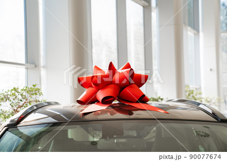 a red gift bow on the roof of a new car in the car dealership.  90077674