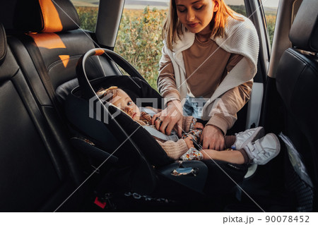 Young Mother Puts Her Baby Daughter in a Child Car Seat in the Car Young Mother Puts Her Baby Daughter in a Child Car Seat in the Car 90078452