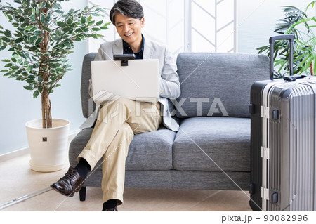 出張中に外出先のソファでリモートワークをするビジネスマン 90082996