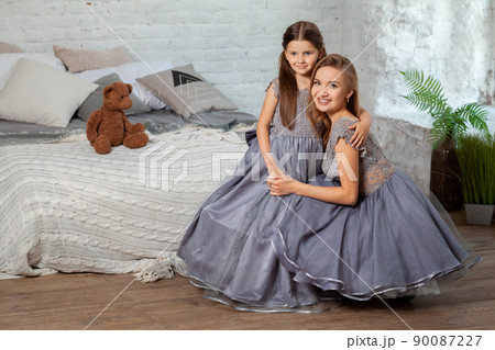 Indoor portrait of a beautiful mother with her charming little daughter posing against bedroom interior. Indoor portrait of a beautiful mother with her charming little daughter posing against bedroom interior. 90087227