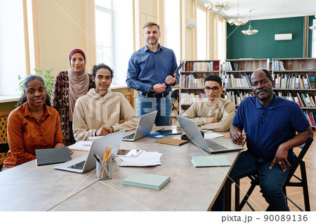 Group portrait of modern English language teacher and multi-ethnic immigrant students having class in library looking at camera 90089136
