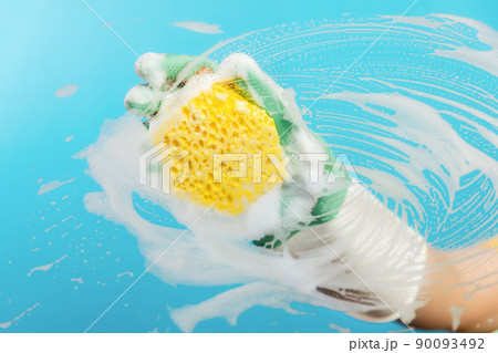 Hand in rubber gloves wipes the glass with a yellow foam sponge. Light blue background. The concept of professional cleaning service Hand in rubber gloves wipes the glass with a yellow foam sponge. Light blue background. The concept of professional cleaning service 90093492