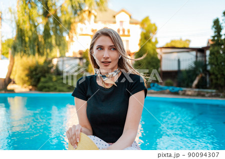 An elegant woman looks away in surprise. In the background there is a pool and a house. Concept of human emotions and expressions 90094307