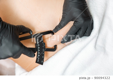 Liposuction. Beautician measures the fat sediments on the client's belly with a caliper. Close up. Aesthetic medicine and plastic surgery 90094322