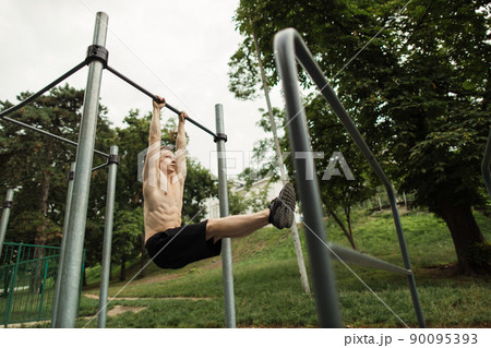 Young caucasian athlete with muscular torso doing corner on crossbar Young caucasian athlete with muscular torso doing corner on crossbar 90095393