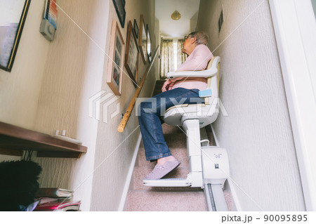 Senior woman using automatic stair lift on a staircase at her home. Medical Stairlift for disabled people and elderly people in the home. Selective focus. Senior woman using automatic stair lift on a staircase at her home. Medical Stairlift for disabled people and elderly people in the home. Selective focus. 90095895