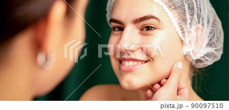 Plastic surgery and beauty concept. Professional cosmetician examining and touching the face of the beautiful young caucasian smiling woman in a clinic of esthetic cosmetology Plastic surgery and beauty concept. Professional cosmetician examining and touching the face of the beautiful young caucasian smiling woman in a clinic of esthetic cosmetology 90097510