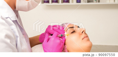 The young white woman is getting rejuvenating facial injections with hyaluronic acid on the eye in a beauty clinic 90097550