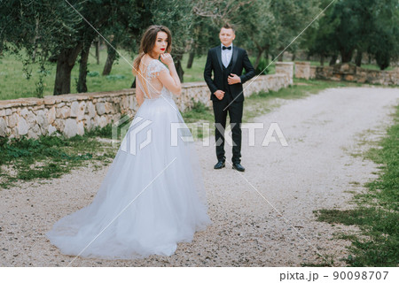 Happy stylish smiling couple walking in Tuscany, Italy on their wedding day. The bride and groom walk down the street by the hands. A stylish young couple walks. Husband and wife communicate nicely Happy stylish smiling couple walking in Tuscany, Italy on their wedding day. The bride and groom walk down the street by the hands. A stylish young couple walks. Husband and wife communicate nicely 90098707