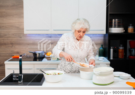 Grandma in the kitchen spreads out steamed salmon and salad on plates Grandma in the kitchen spreads out steamed salmon and salad on plates 90099339