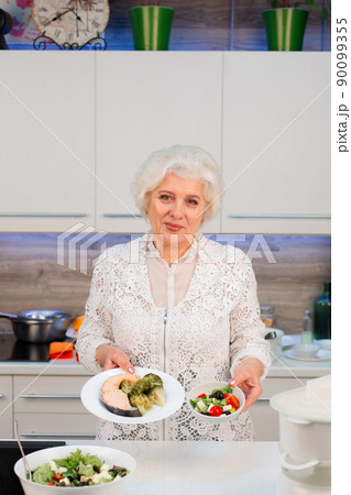 A pensioner cooks healthy food in the kitchen, demonstrates cooked dishes A pensioner cooks healthy food in the kitchen, demonstrates cooked dishes 90099355