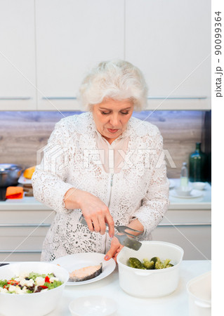 Grandma spreads healthy food on plates of steamed red fish and broccoli Grandma spreads healthy food on plates of steamed red fish and broccoli 90099364