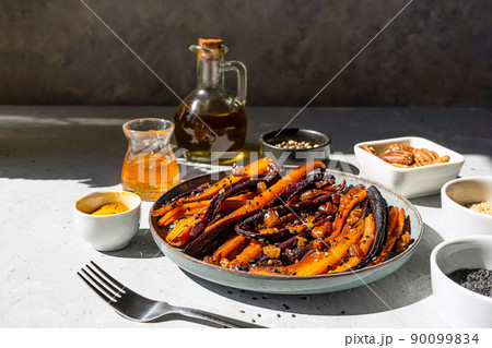 Roasted glazed spicy violet and orange carrots with ingredients on grey background. Close up Roasted glazed spicy violet and orange carrots with ingredients on grey background. Close up 90099834