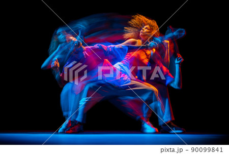 Young man and woman dancing hip-hop in sportive style clothes on dark background at dance hall in mixed neon light. Youth culture, hip-hop, movement 90099841
