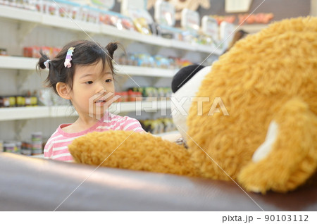 cute little girl looks at the bear doll on the sofa with back view 90103112