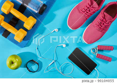 Flat lay shot of Sport equipment. Sneakers, water, earphones and phone on blue background. 90104055