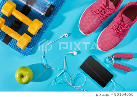 Flat lay shot of Sport equipment. Sneakers, water, earphones and phone on blue background. 90104056