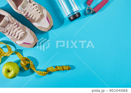 Sneakers with measuring tape on cyan blue background. Centimeter in yellow color near white trainers, close up. 90104066