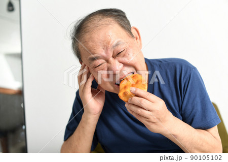 辛い表情で煎餅を食べる高齢者の男性 90105102